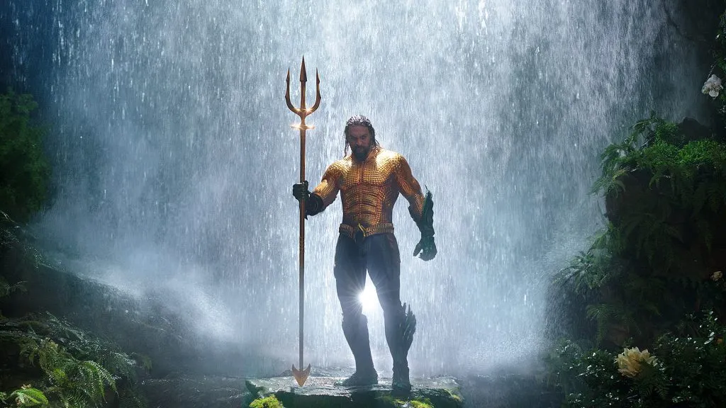 Jason Momoa jako Aquaman trzymający trójząb pod wodospadem w filmie DC Aquaman.