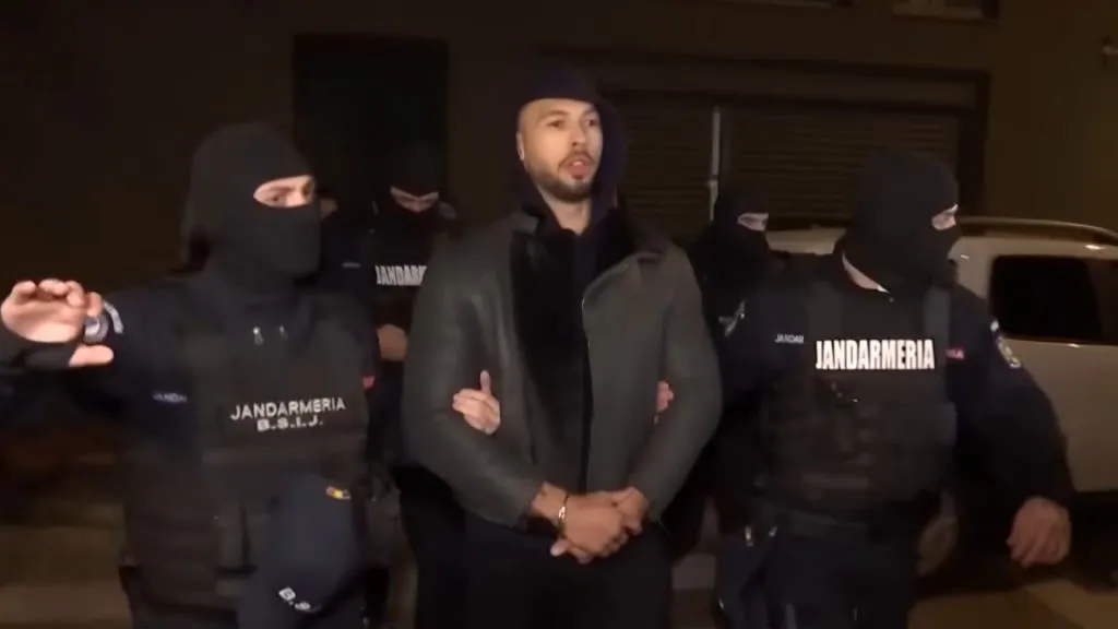 Andrew Tate in schwarzer Jacke wird von der Polizei festgehalten