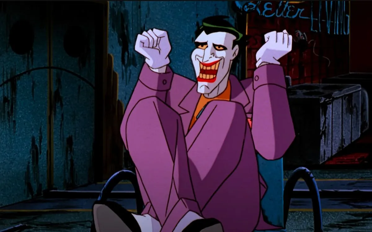 An animated Joker sits on the ground cross-legged and laughing in