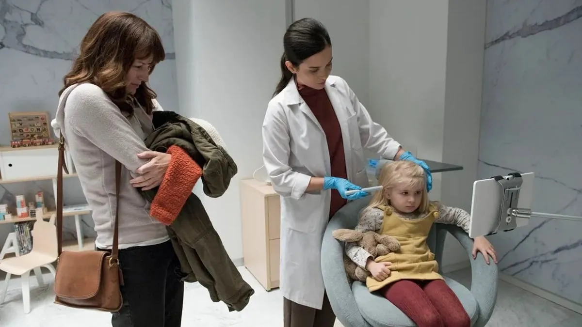 A worried mother watches as a doctor injects her daughter