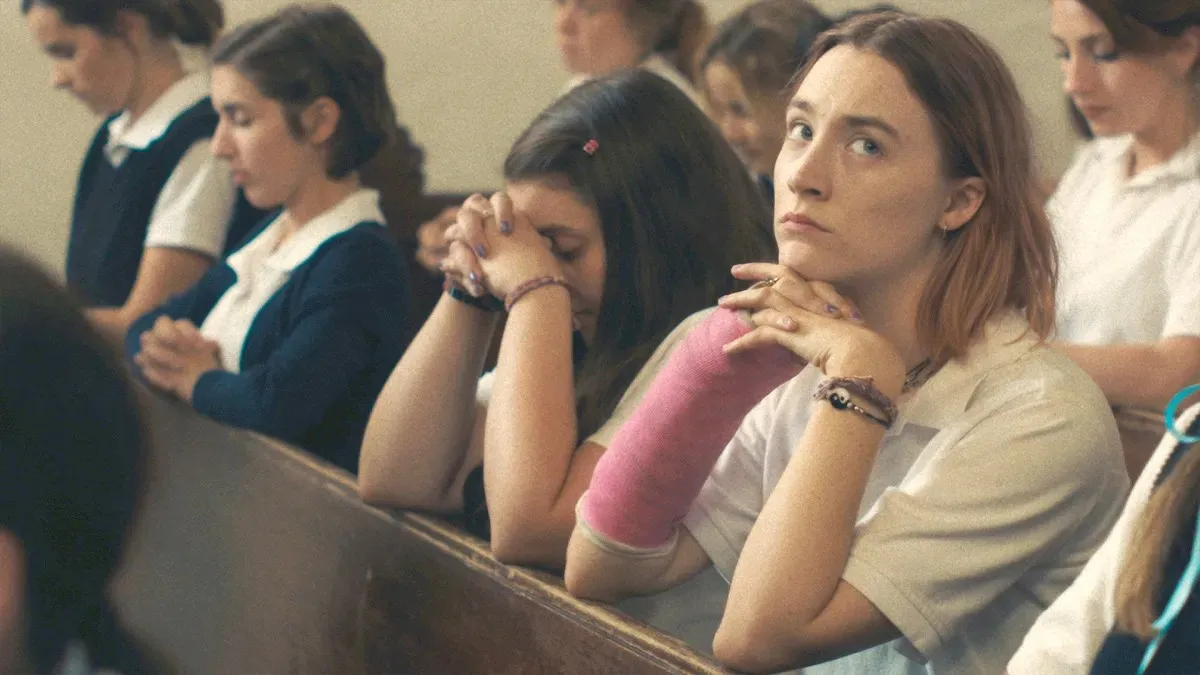 Lady Bird ajoelha-se em uma igreja parecendo distraída