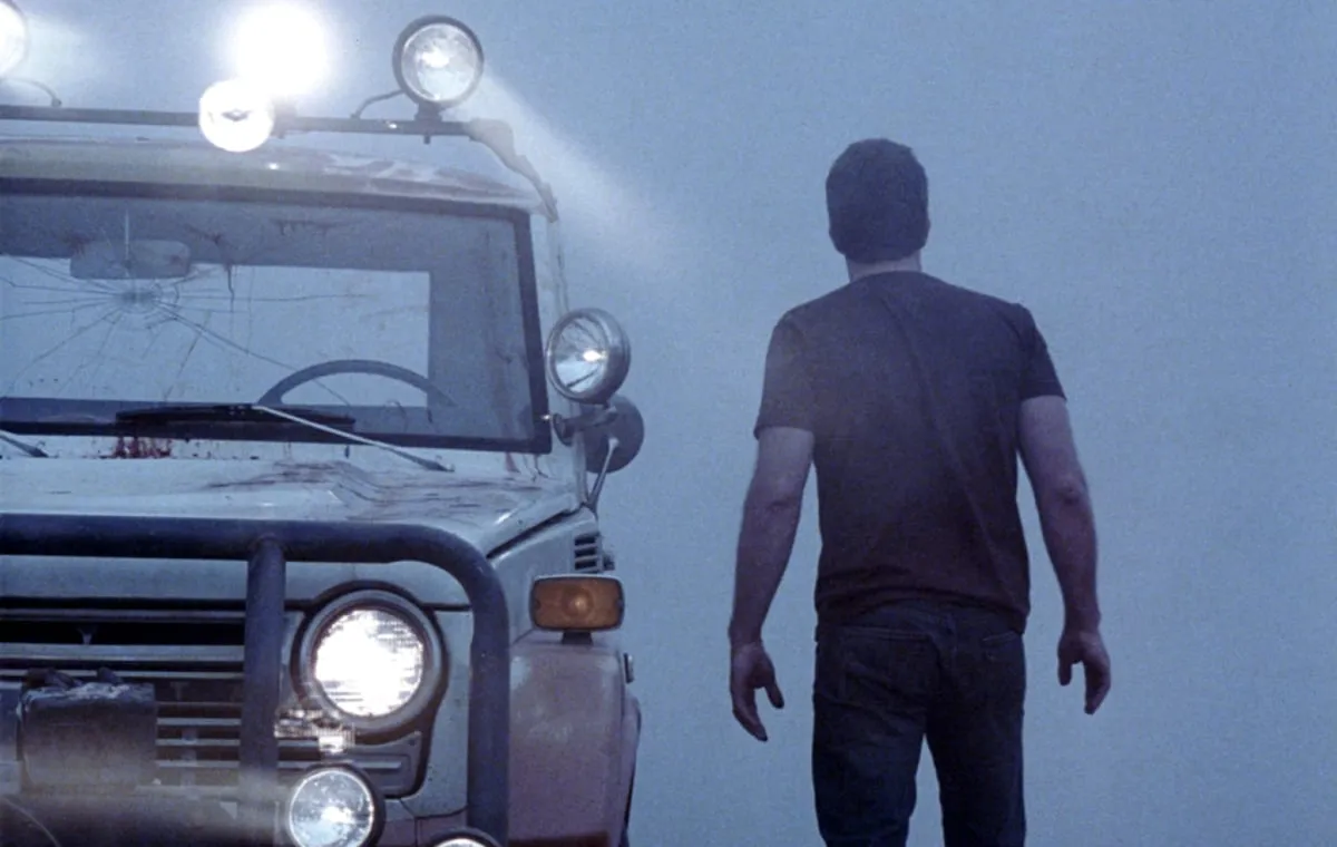 Un homme regarde dans un épais brouillard à côté de son camion dans « The Mist »