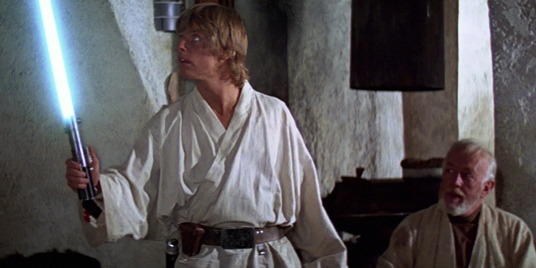 Luke tenant un sabre laser pendant qu'Obi-Wan regarde dans Star Wars Un nouvel espoir