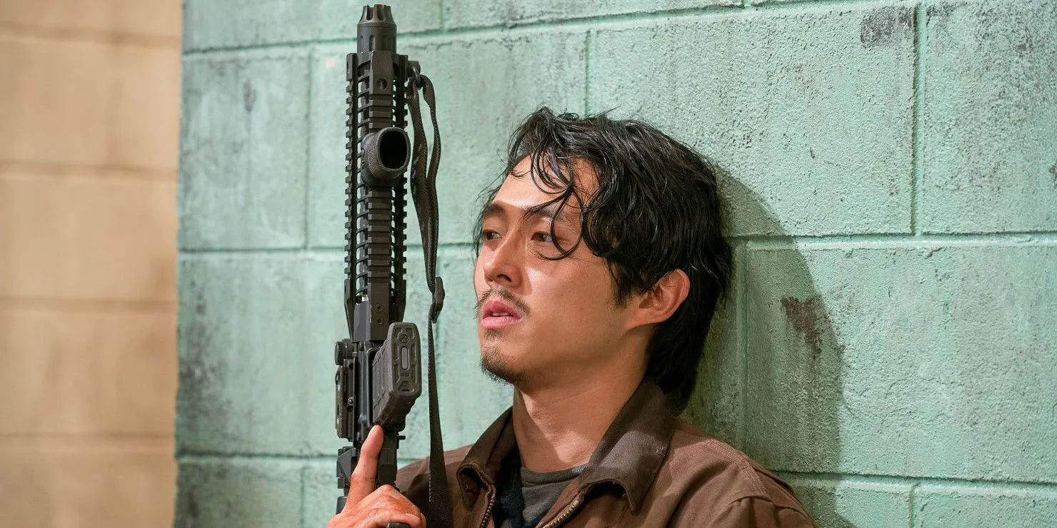 Glenn Rhee encostado na parede enquanto segura uma arma em The Walking Dead