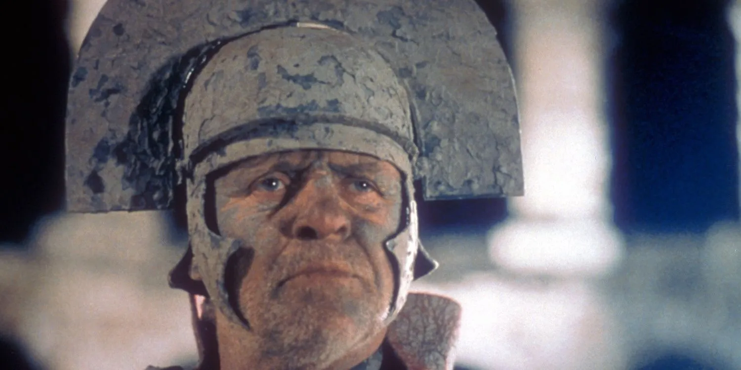 Anthony Hopkins como Titus Andronicus coberto de lama e usando um capacete em Titus 1999