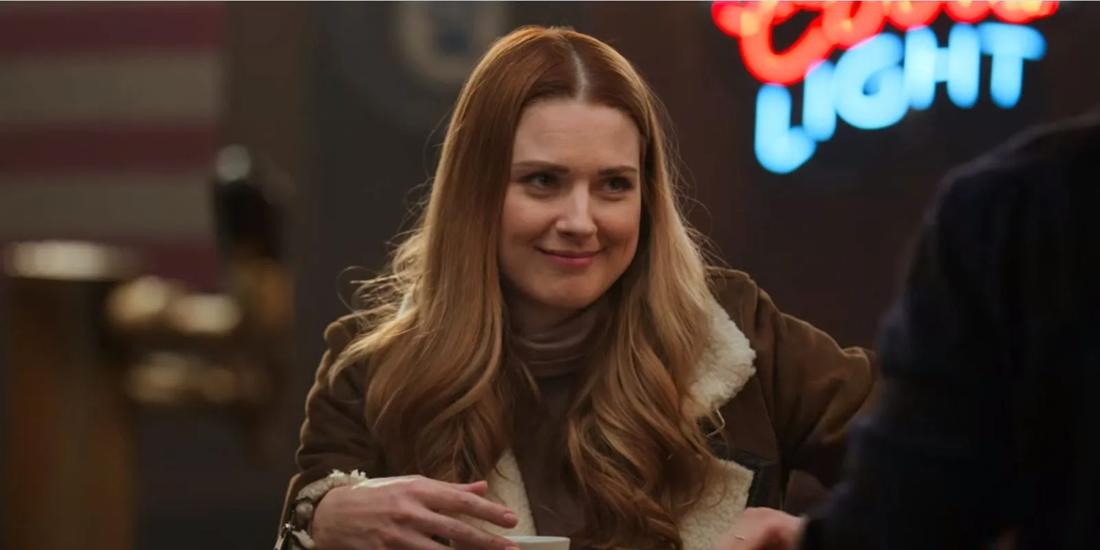 Alexandra Breckenridge sentada a la mesa en un bar en Virgin River.