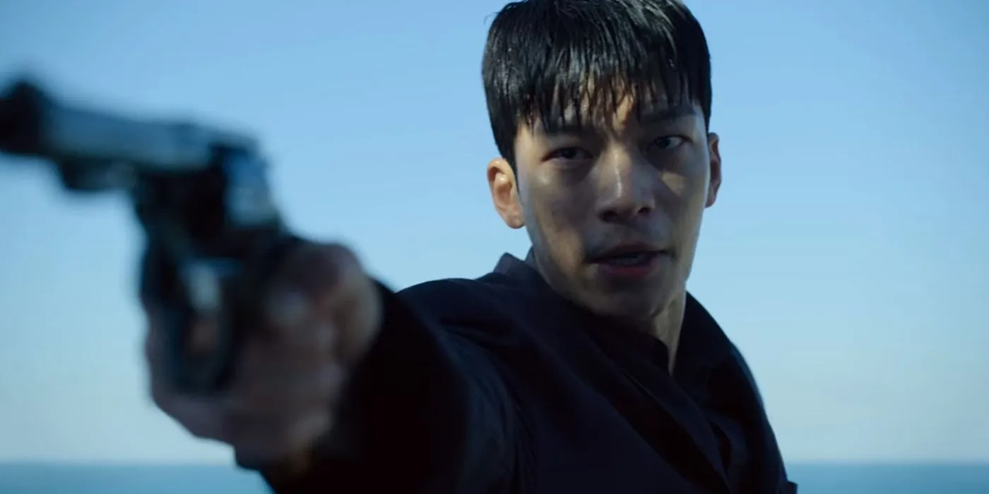 Jun-ho aims his gun against a blue sky and ocean