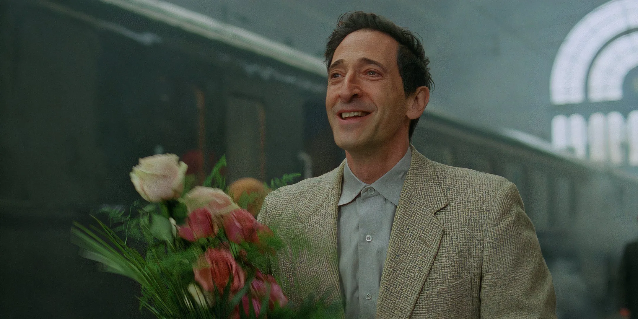 Adrien Brody en The Brutalist sosteniendo flores en la estación de tren