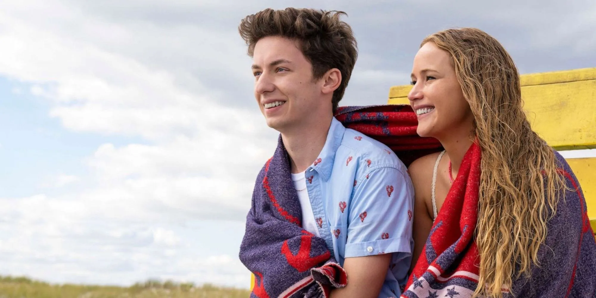 Maddie (Jennifer Lawrence) et Percy (Andrew Barth Feldman) ont une serviette autour d'eux, alors qu'ils sont assis à la plage dans No Hard Feelings.