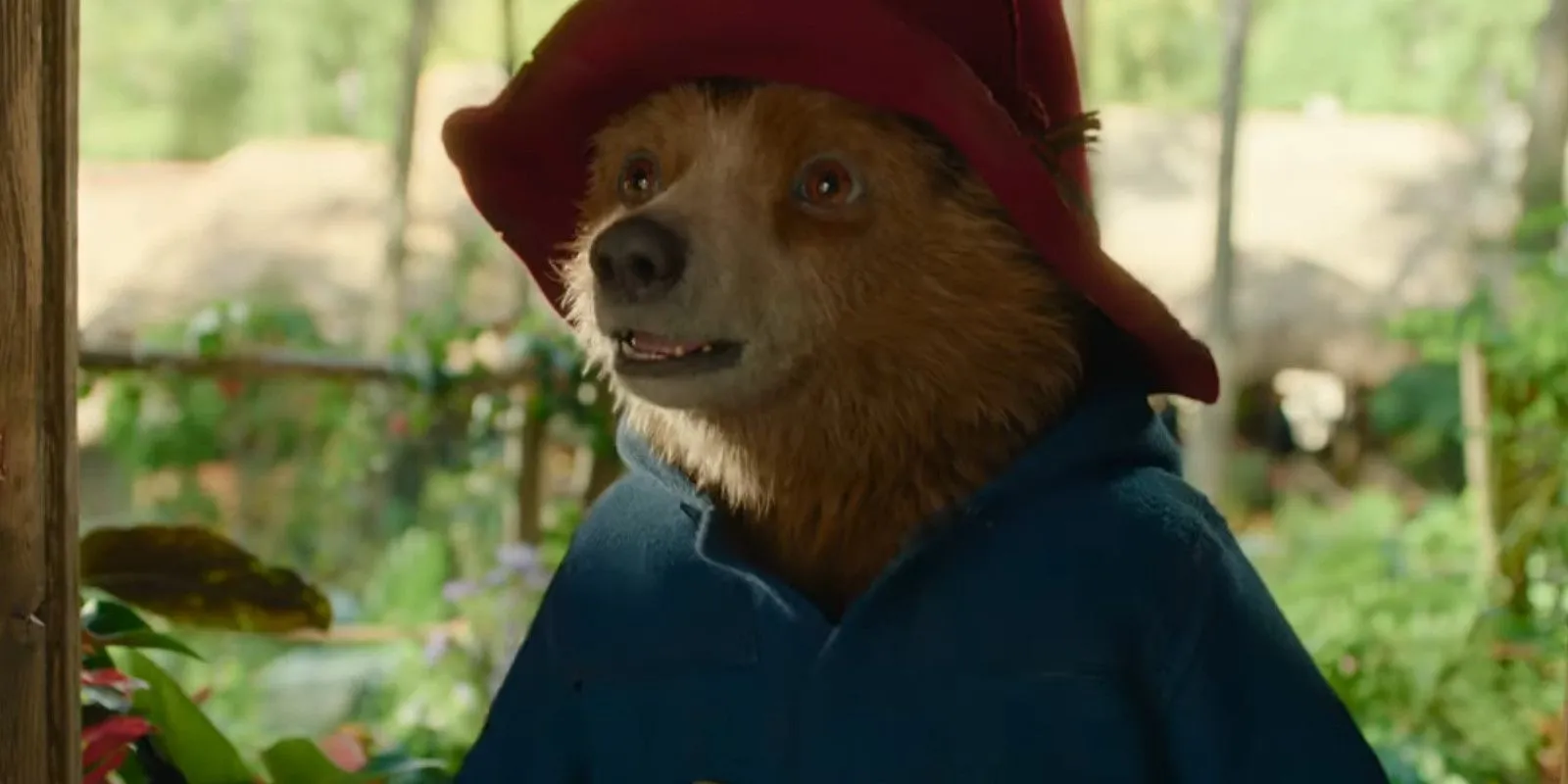 L'ours Paddington souriant dans une porte, avec de la verdure derrière lui, tout en portant sa tenue classique dans Paddington au Pérou