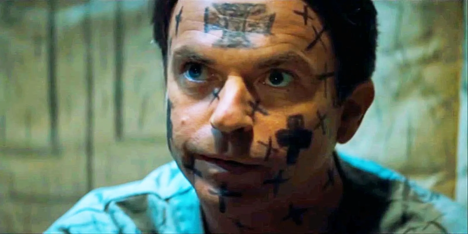 Sam Neill em um asilo com cruzes desenhadas sobre o rosto em In The Mouth of Madness