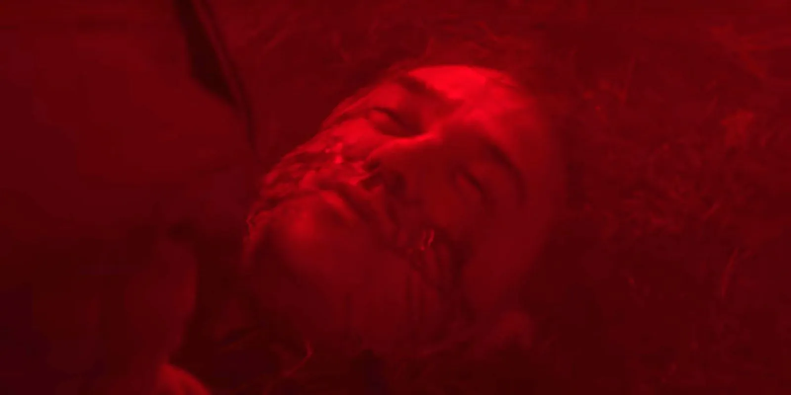 Doctor Boone laying on the forest ground with a flare illuminating the scene in red from The Silencing.