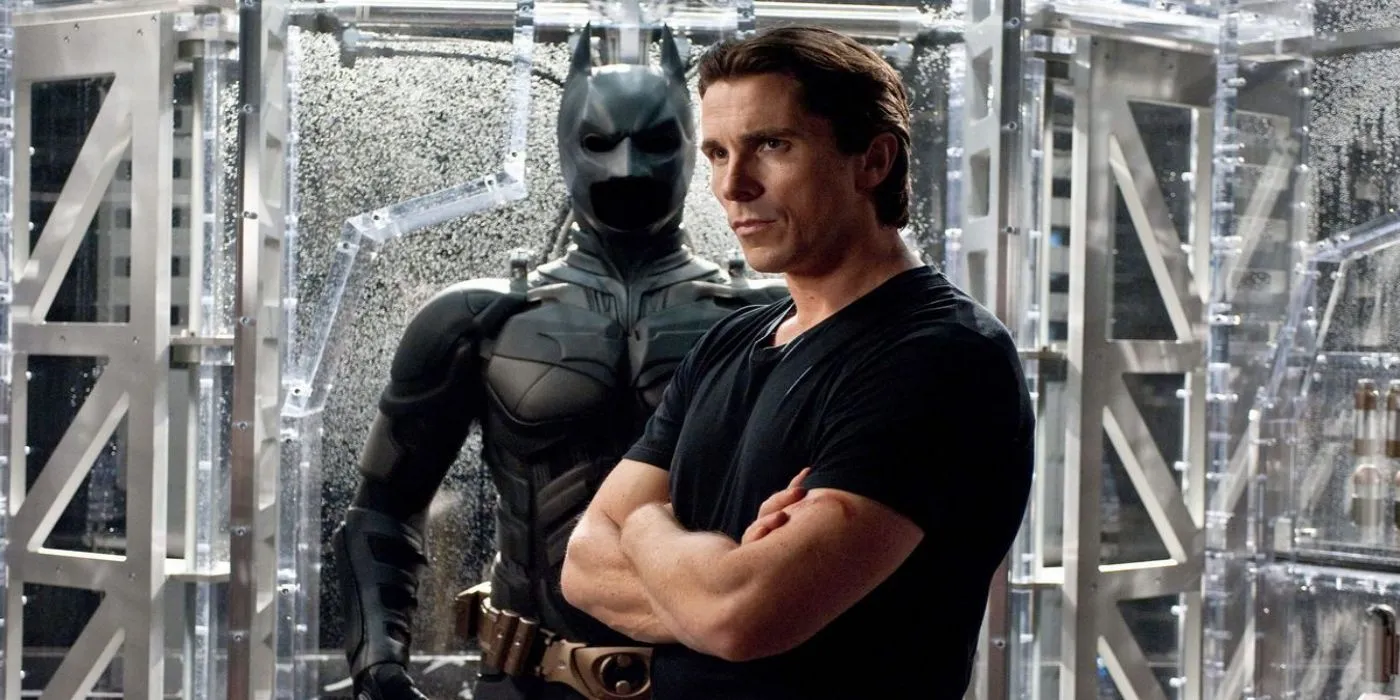 Christian Bale nei panni di Bruce Wayne è in piedi davanti al suo costume di Batman in The Dark Knight