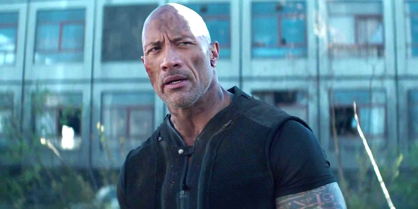 Dwayne Johnson dans le rôle de Luke Hobbs couvert de poussière et semblant sceptique dans Hobbs and Shaw