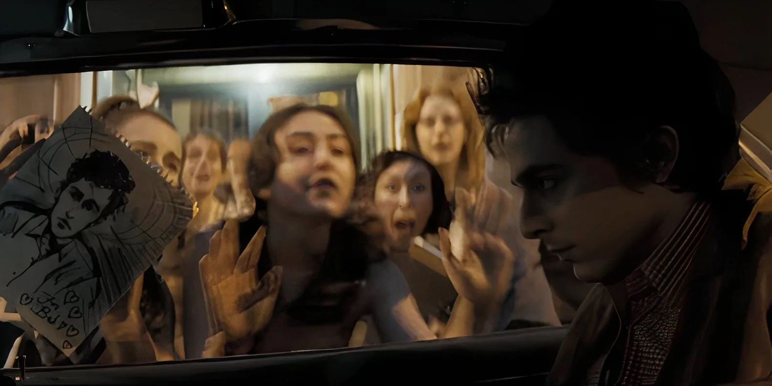 Bob Dylan sitting in a car surrounded by fans in A Complete Unknown Bob Dylan sitting in a car surrounded by fans in A Complete Unknown