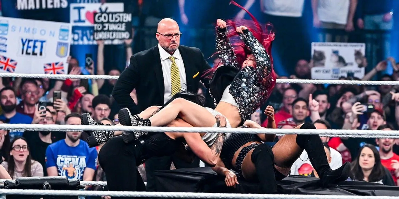 Adam Pearce watches Iyo Sky get powerbombed by Rhea Ripley onto Bianca Belair on a table on WWE Monday Night Raw