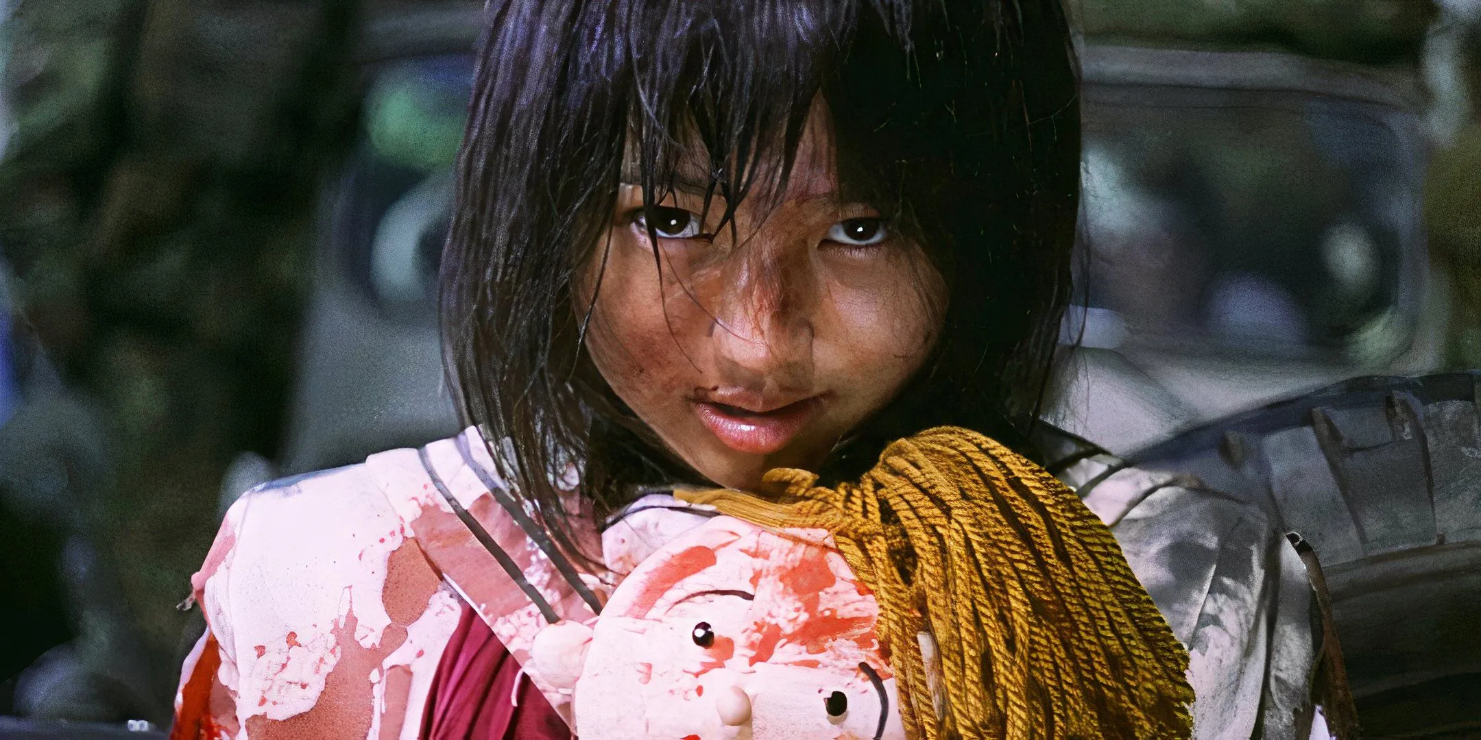 Covered in blood, Ai Iwamura holds a doll and looks at the camera with a blank expression. Covered in blood, Ai Iwamura holds a doll and looks at the camera with a blank expression.