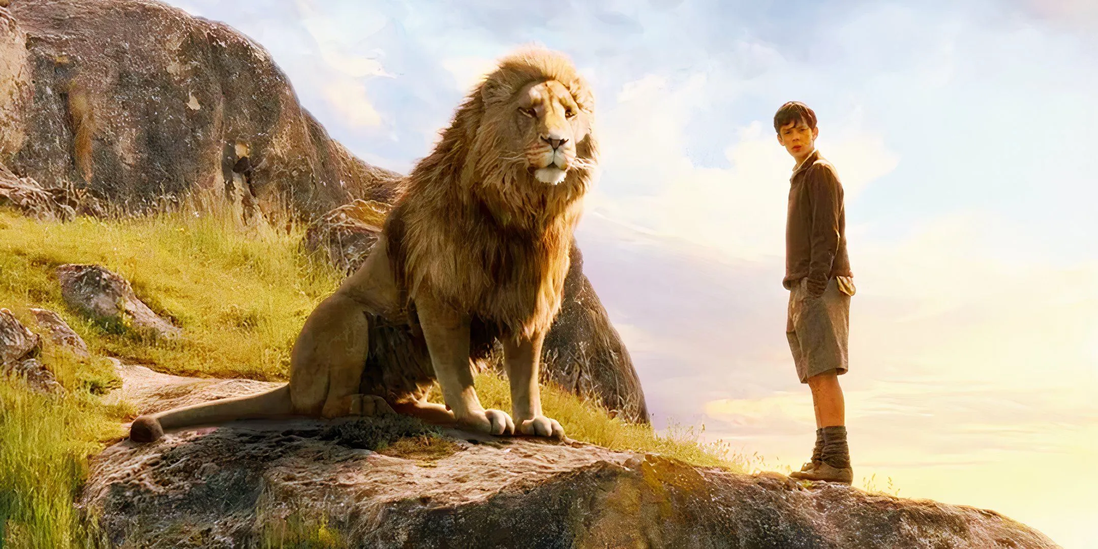 Aslan the lion sits with a boy on a hill in The Chronicles of Narnia franchise