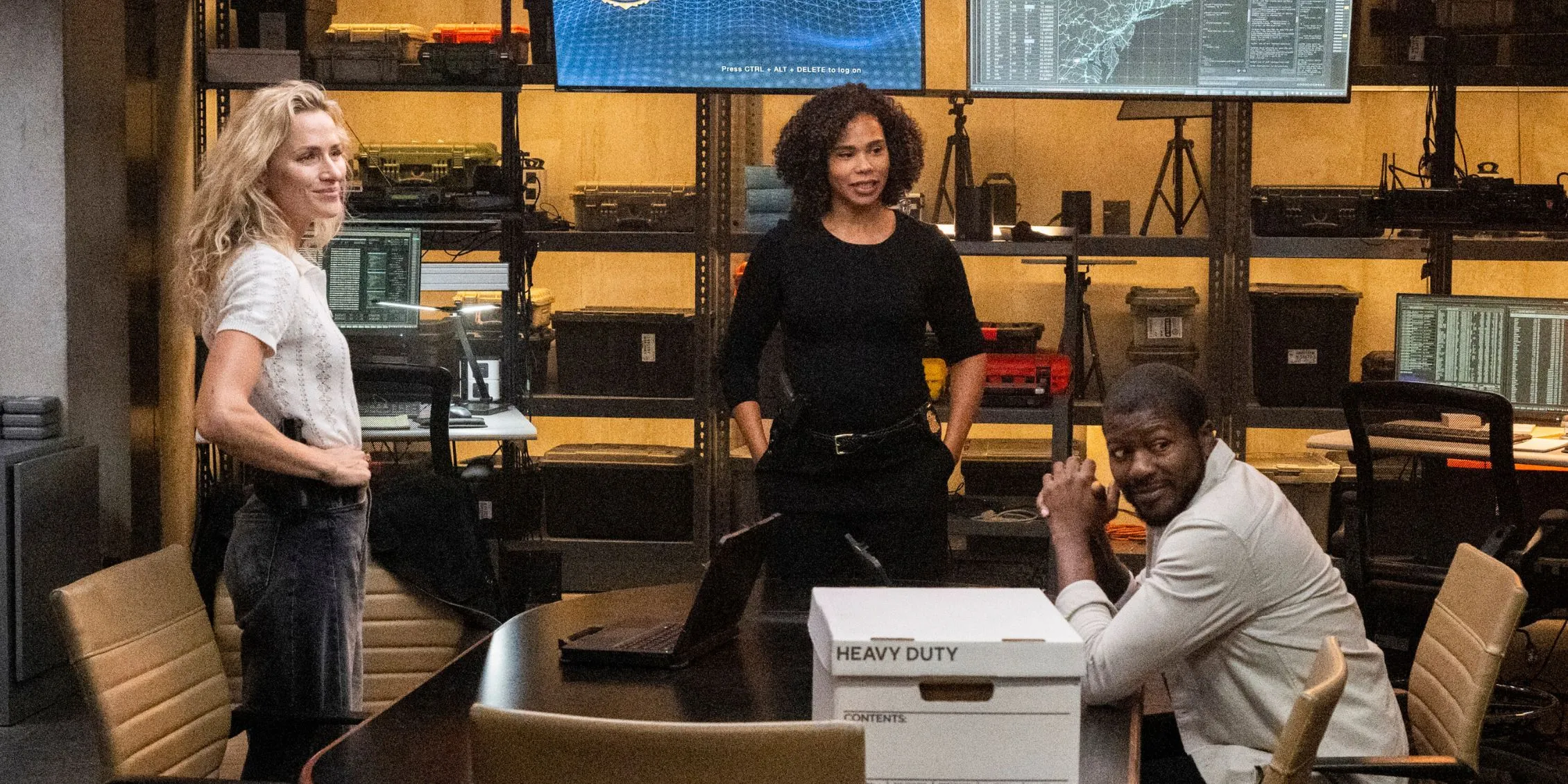 Ray sitting at a table with a file box while Nina and Barnes are standing near him in FBI: Most Wanted Ray sitting at a table with a file box while Nina and Barnes are standing near him in FBI: Most Wanted