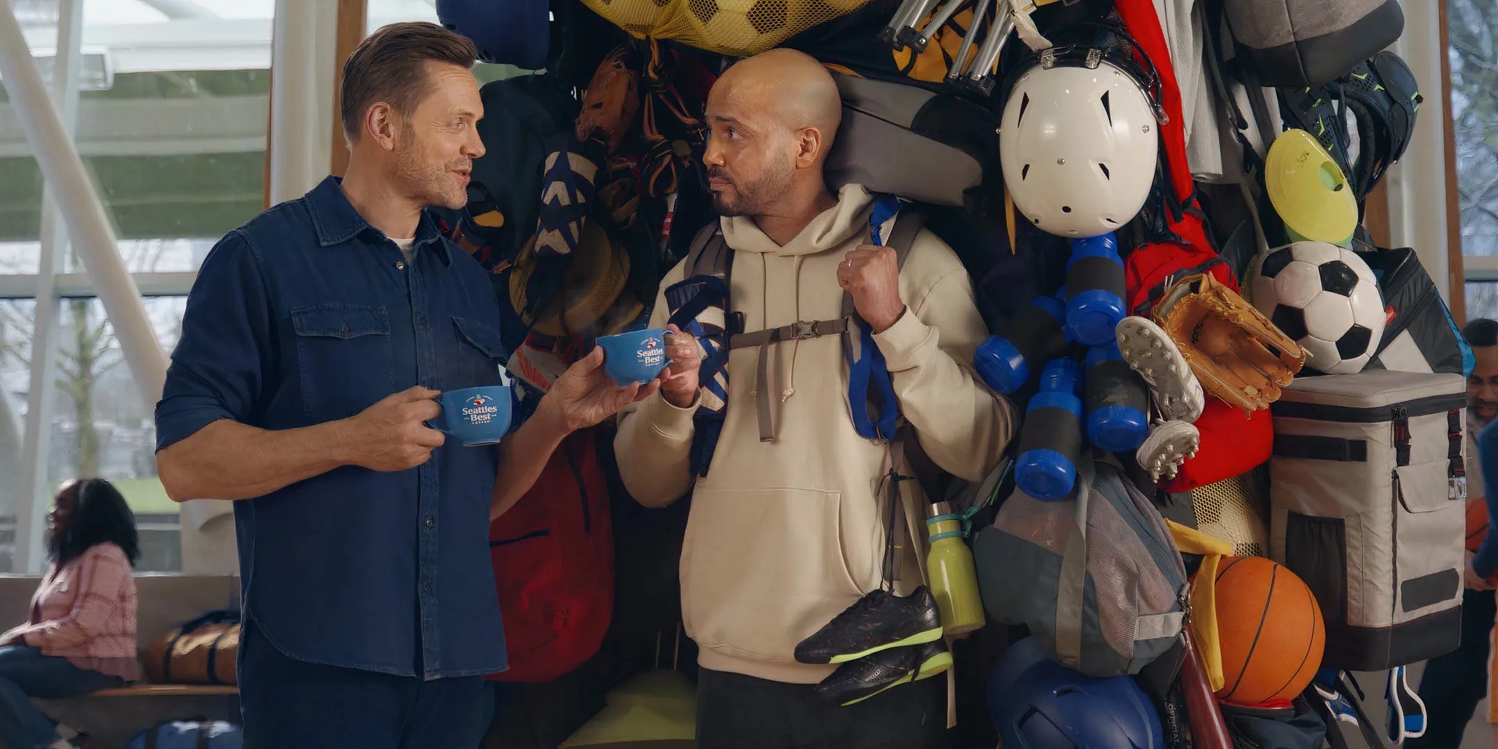 Joel McHale handing a Seattle's Best Coffee mug to a man with a large backpack Joel McHale handing a Seattle's Best Coffee mug to a man with a large backpack