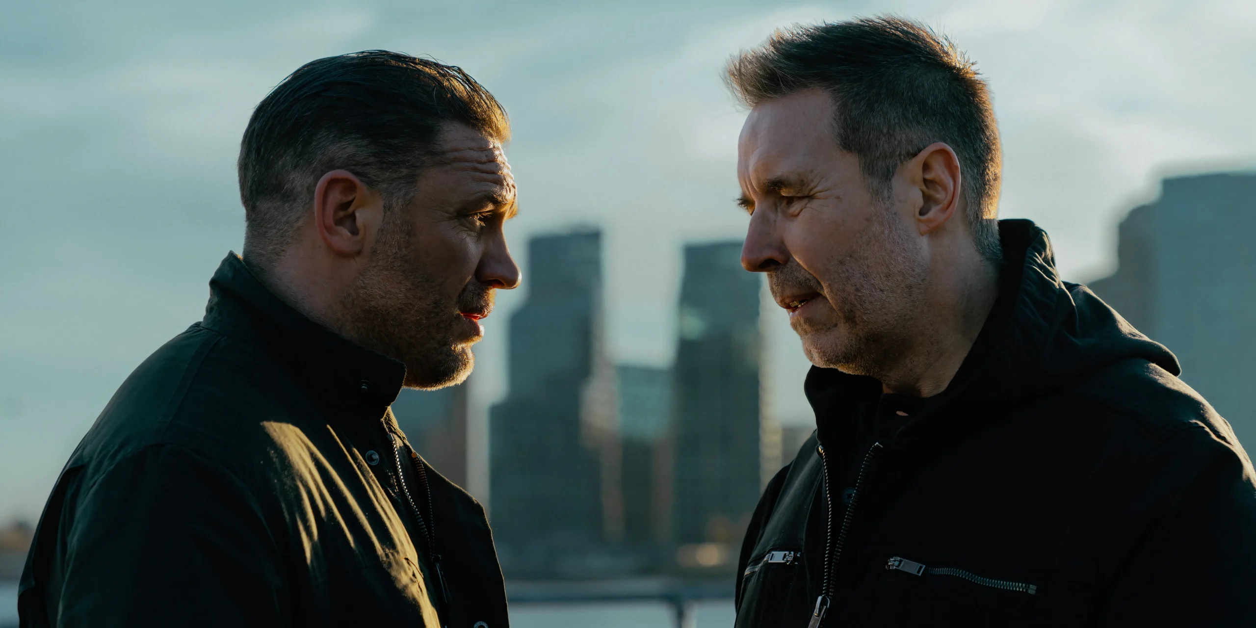 Harry talks closely with Kevin while standing in front of the city skyline in MobLand season 1.