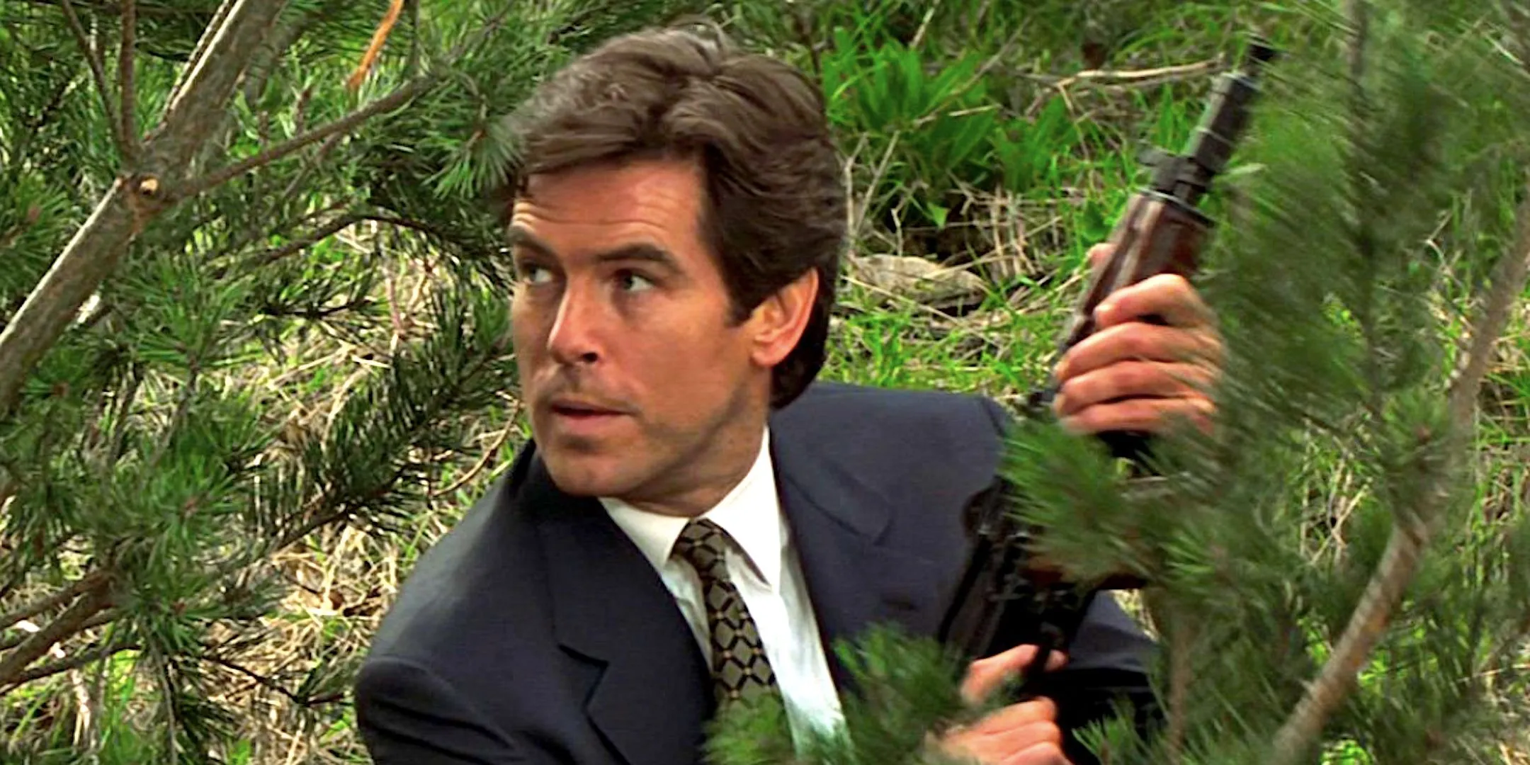 Pierce Brosnan's James Bond crouches among tree branches holding a gun in GoldenEye Pierce Brosnan's James Bond crouches among tree branches holding a gun in GoldenEye