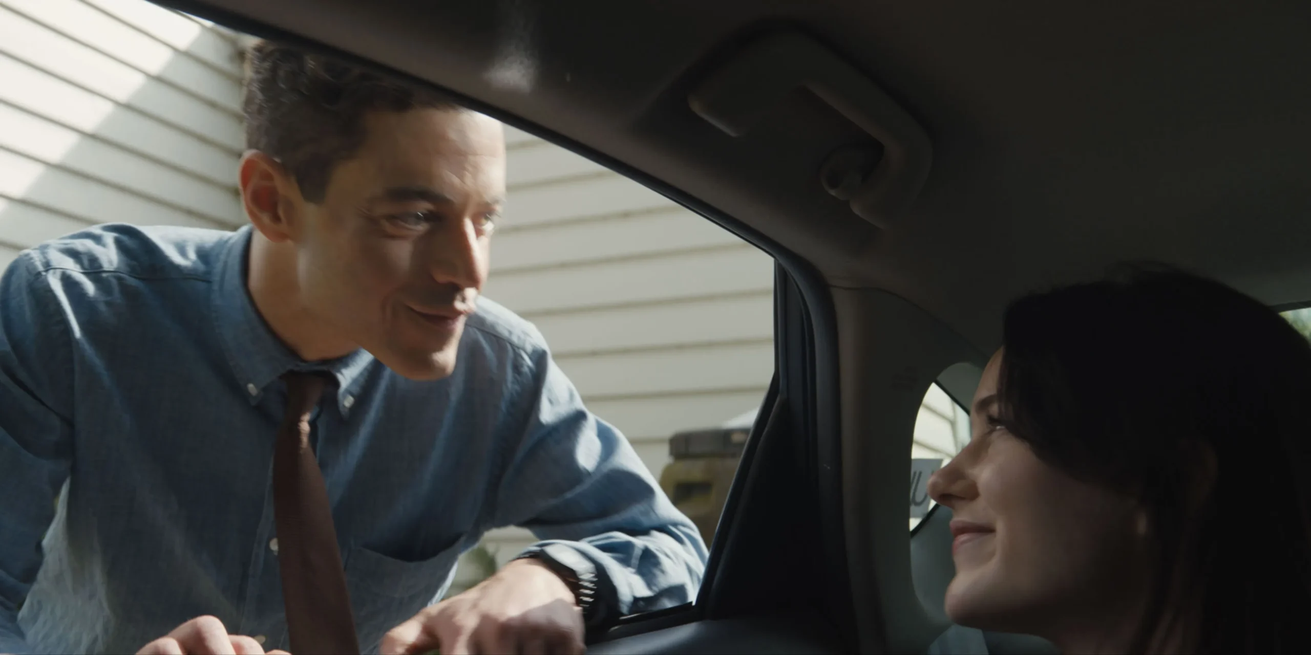 Rami Malek leaning into Rachel Brosnahan's car window in The Amateur Rami Malek leaning into Rachel Brosnahan's car window in The Amateur