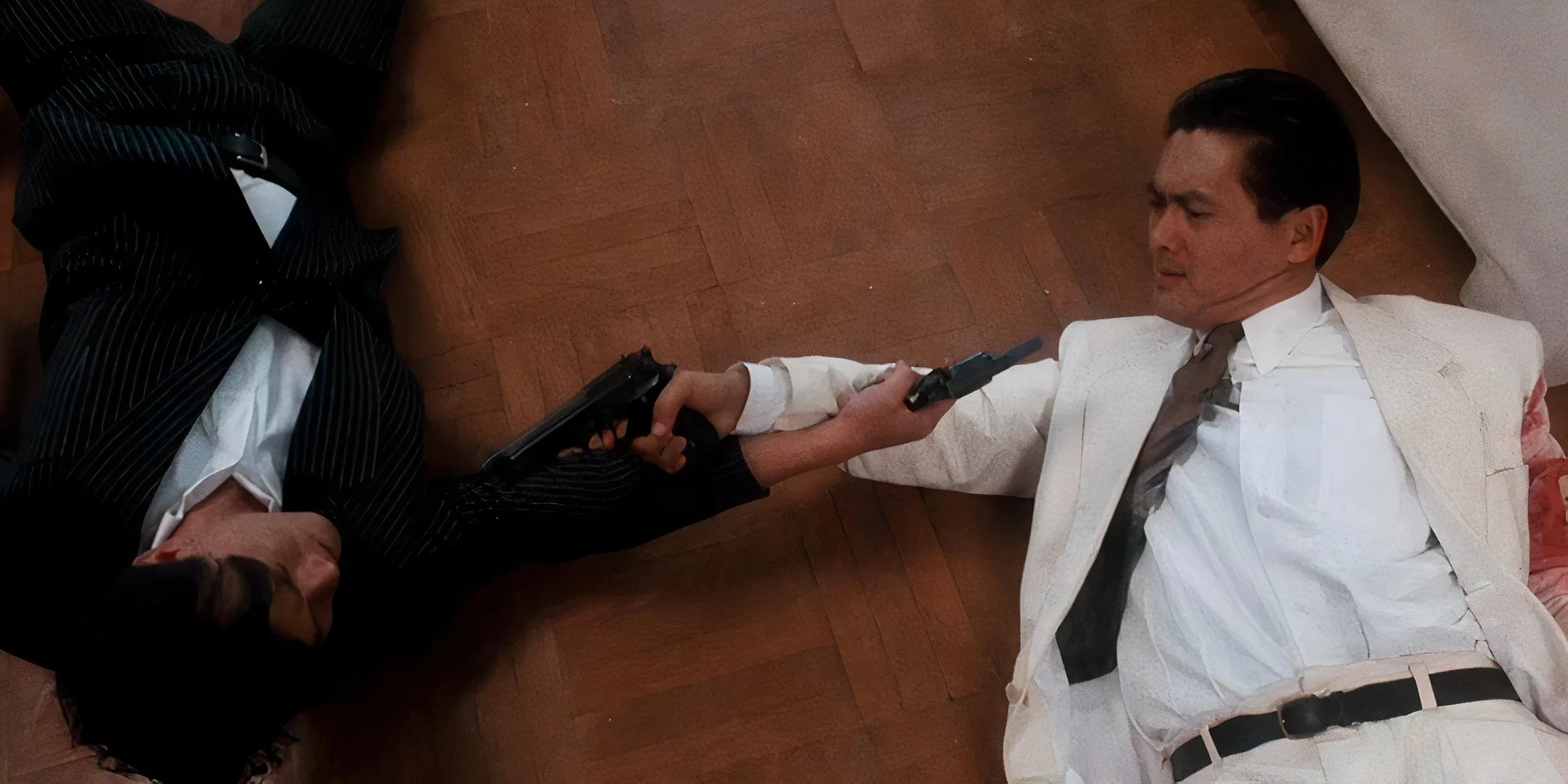 Two men are lying on the floor pointing guns at one another. Two men are lying on the floor pointing guns at one another.