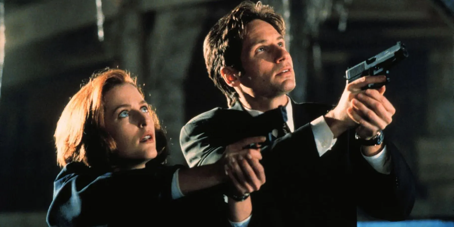 Dana Scully (Gillian Anderson) and Fox Mulder (David Duchovny) aiming their guns upward. Dana Scully (Gillian Anderson) and Fox Mulder (David Duchovny) aiming their guns upward.