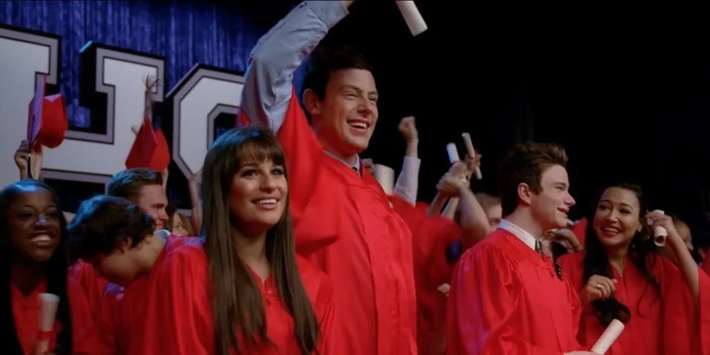 Finn, Rachel, Santana, and Kurt celebrating in their red graduation robes in Glee Season 3.